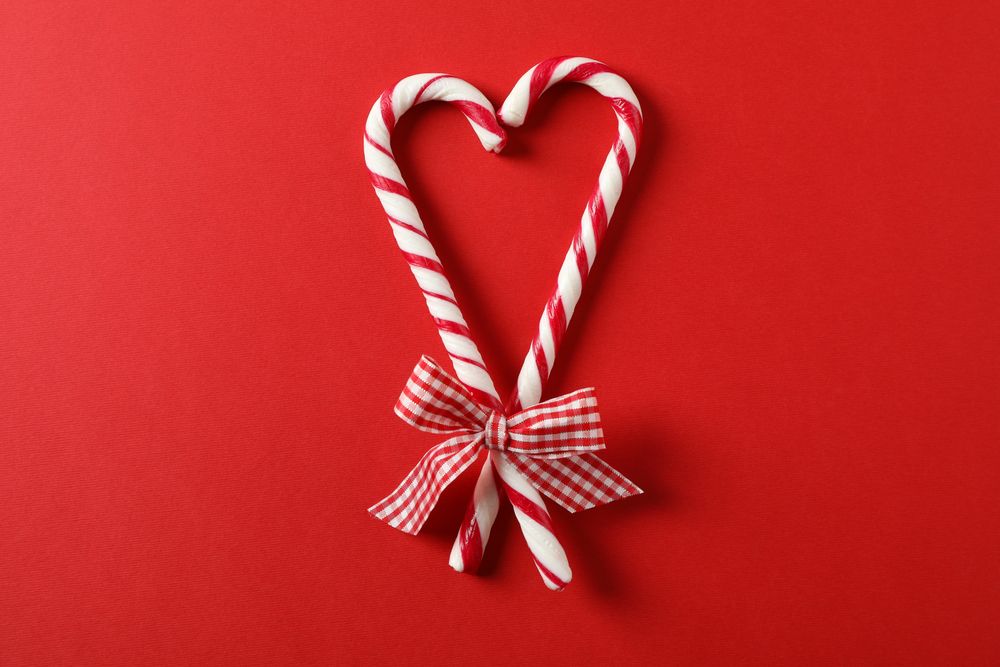 Sweet candy canes with bow on red background, space for text