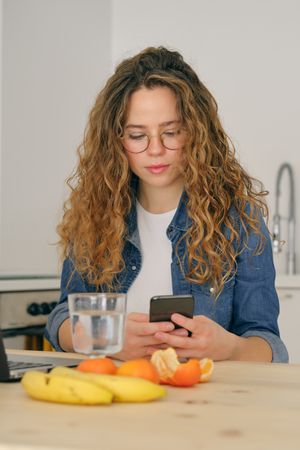 Young woman sitting with smartphone in kitchen