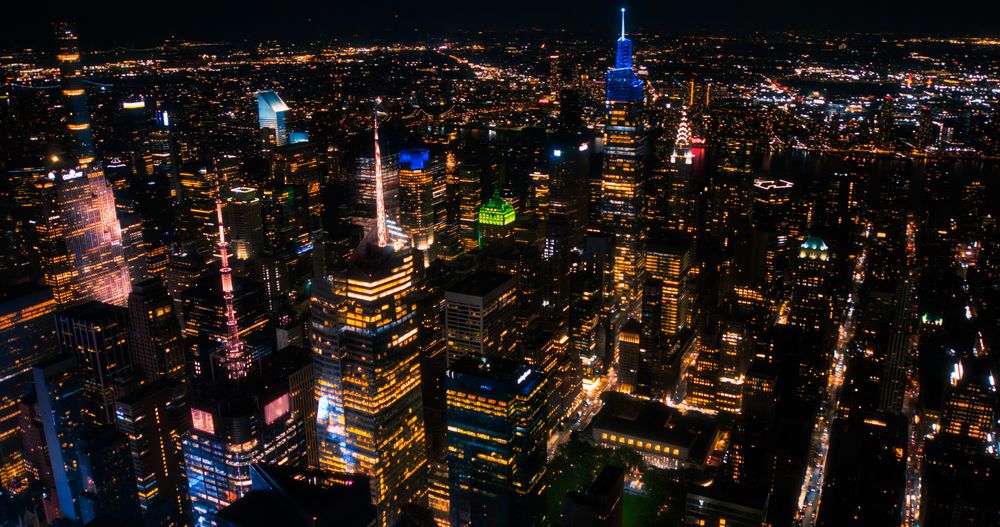 Aerial Shot of Office Buildings at Night. Rooms Have Lights On, Businesspeople and Managers Working Long Hours in New York City. Helicopter Cityscape View of Manhattan in the Evening