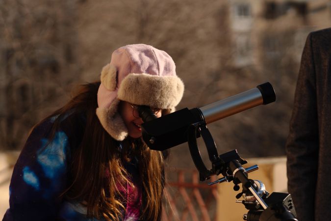 Young astronomer in pink winter hat examines specialized solar telescope