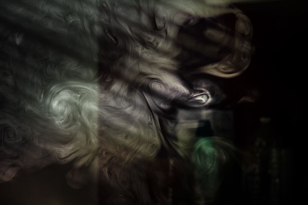 Swirls of smoke in a dark room with light coming in through the blinds