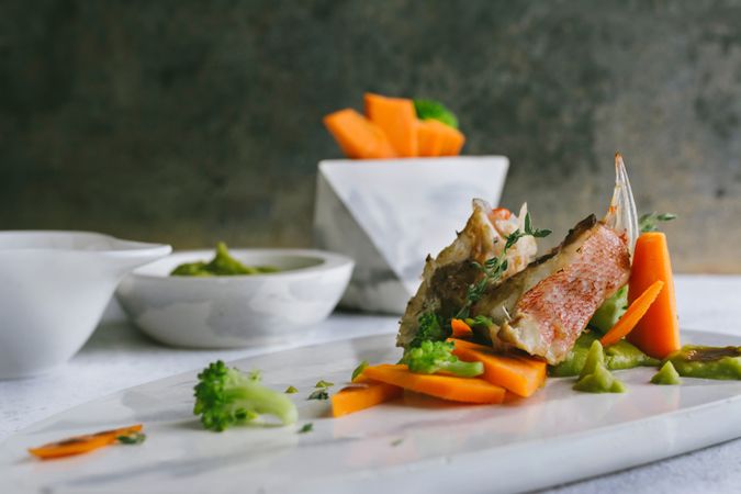 grilled scorpion fish with mashed peas and carrot sticks, on a marble plate