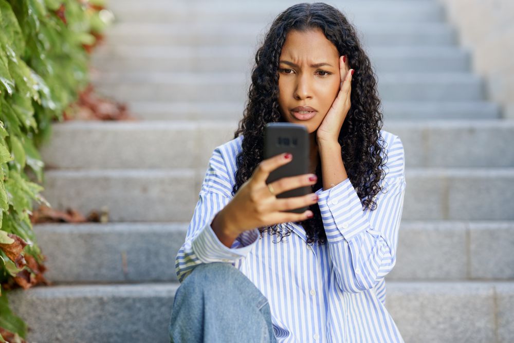 A worried woman sits on the steps, anxiously looking at her phone amid vibrant city life