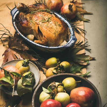 Roast turkey in decorative roasting pan, on table with fall leaves and fruit, square crop