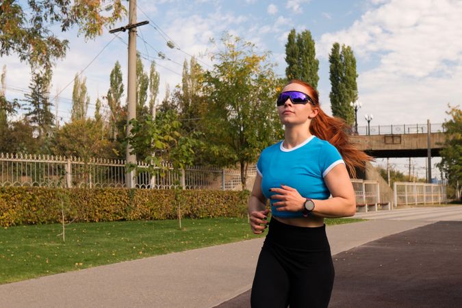 Woman jogging in park, wearing sunglasses and sportswear.