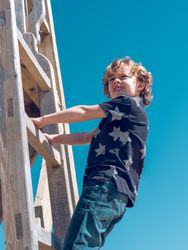 Delightful child standing on wooden ladder of playground
