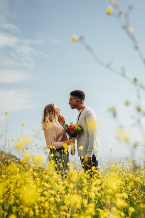 Side view of young man looking at his girlfriend holding flowers outdoors