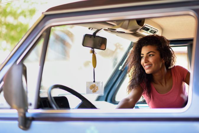 Female in pink t-shirt with curly hair sitting up in passenger side of vehicle
