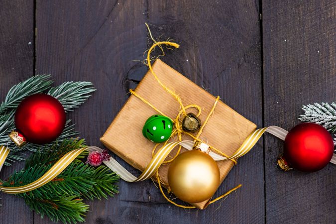 Top view of Christmas gift wrapped in brown paper surrounded by baubles