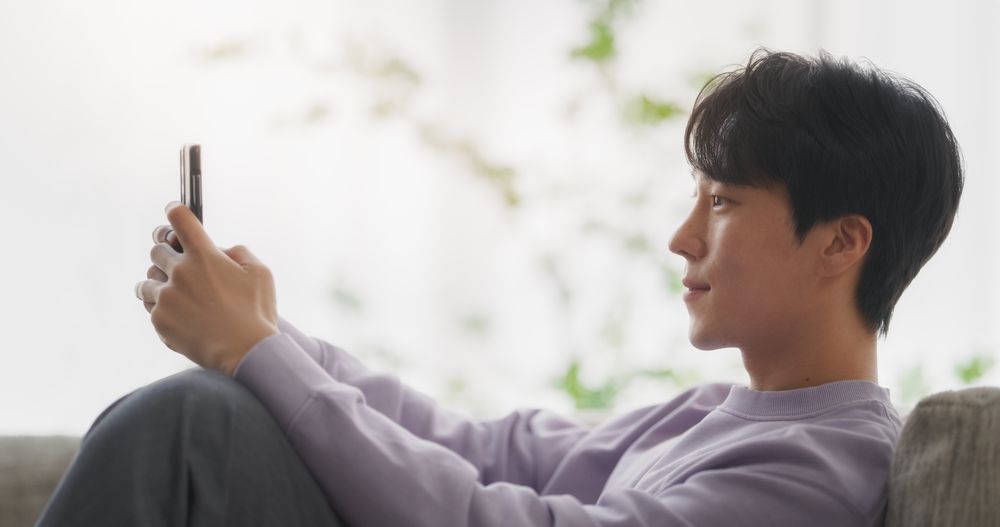 South Korean Young Man Enjoying His Leisure Time while Relaxing and Using a Smartphone.