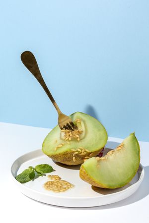 Sliced small melon on plate with spoon and fork