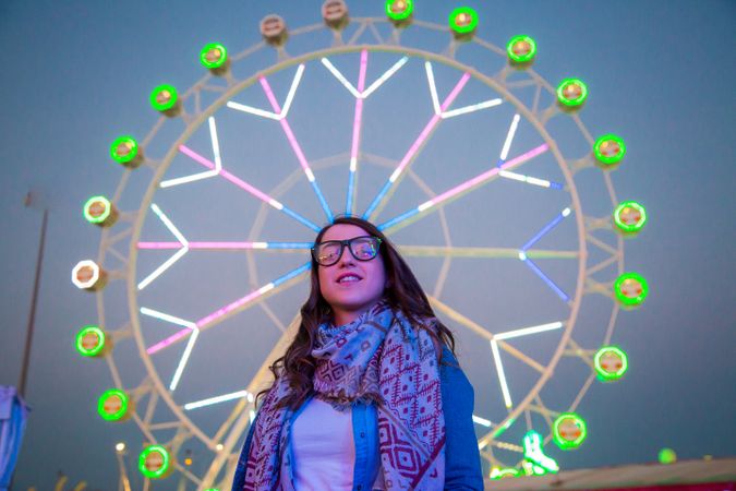 Smiling young woman near illuminated ferris wheel at night