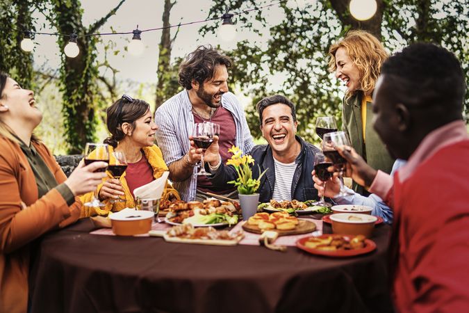 Company of happy people chatting & dining at the barbecue table relaxing together eating grilled food