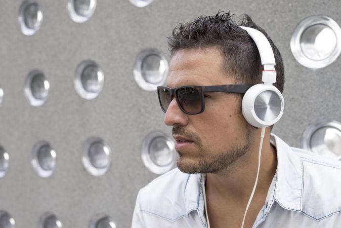 Male in sunglasses listening to something on phone while sitting in front of patterned cement wall