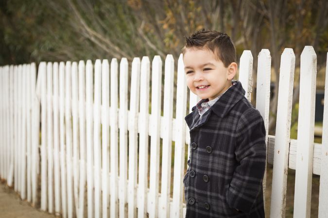 Young Boy Waiting For School Bus Along Fence Outside.