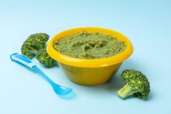 Bowl with broccoli puree on blue background, top view