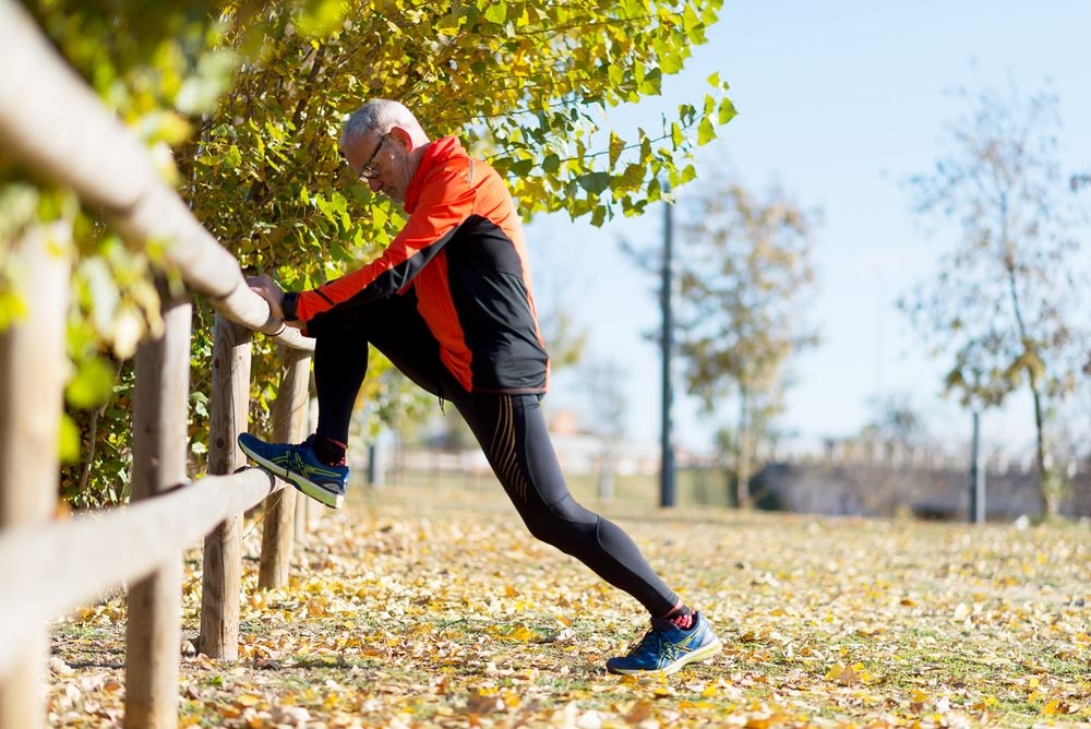 Side view of male stretching legs on wooden fence