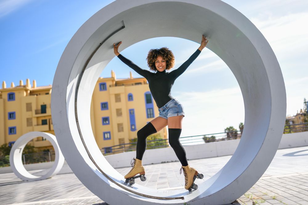 Woman in roller skates, dark top and jean shorts posing inside of sculpture