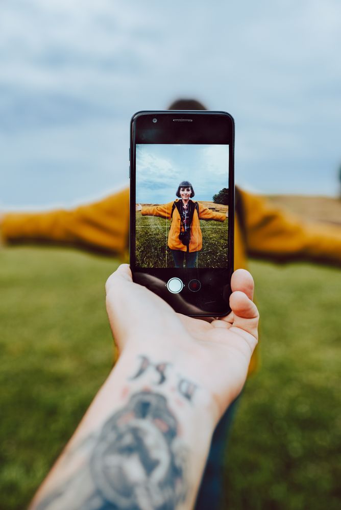 Crop hand taking photo of woman in field
