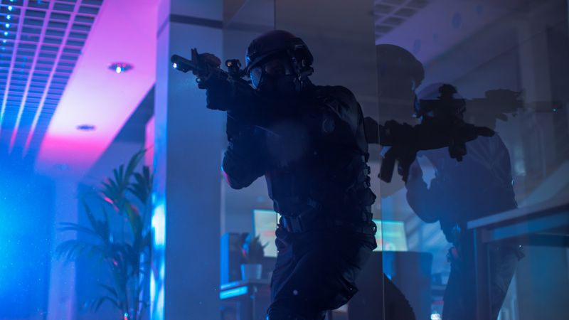 Masked Team of Armed SWAT Police Officers Move in a Hall of a Dark Seized Office Building with Desks and Computers.