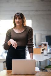 Transgender woman standing at table with laptop
