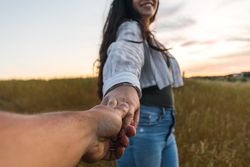 couple holding hands in a field at sunset