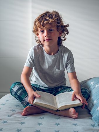 Cute boy sitting on bed with opened book