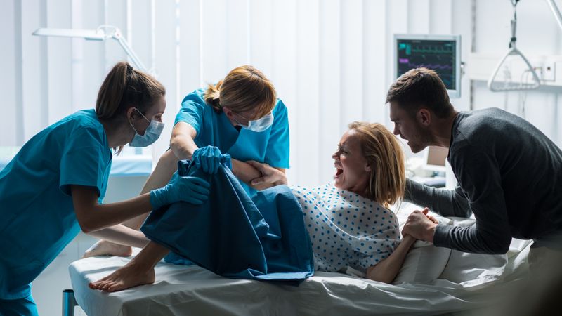 In the Hospital Woman in Labor Pushes to Give Birth, Obstetricians Assisting, Spouse Holds Her Hand