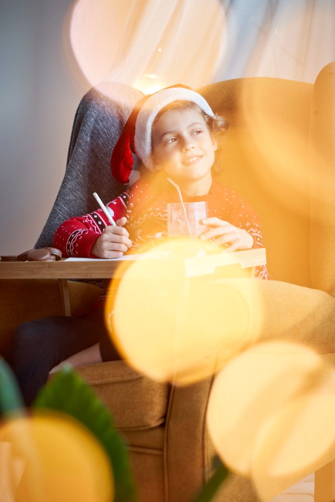 Dreamy boy in Santa hat writing on paper