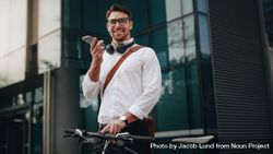 Smiling businessman talking over mobile phone standing on street with his bicycle 56olj4