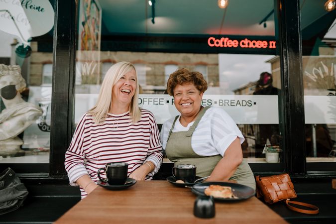 Two older woman smiling with coffee and tea at cafe