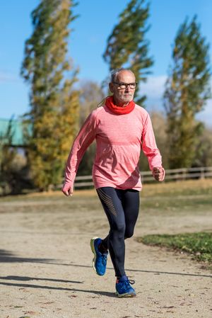 Grey haired man in red shirt and glasses exercising outside looking forward