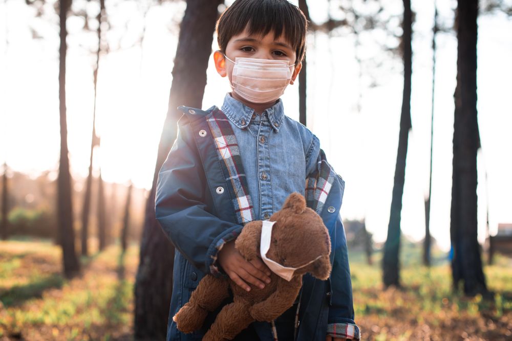 Boy holding teddy bear standing in woods