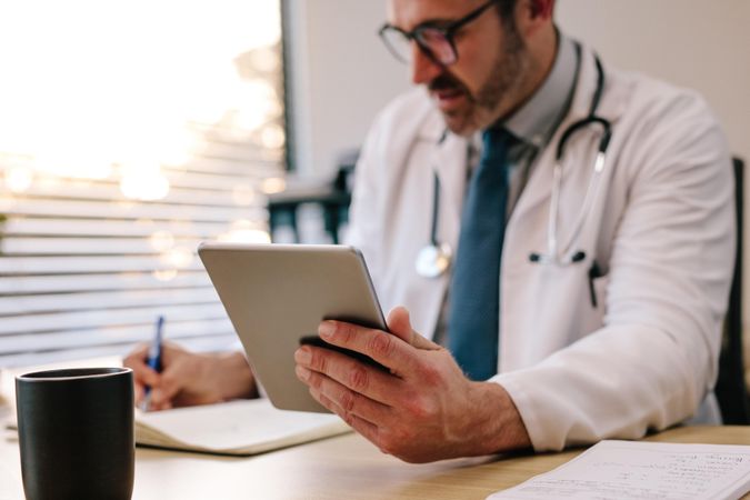 Focus on digital tablet in hand of doctor sitting at his desk