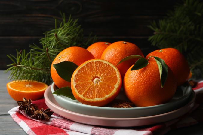 Plates with mandarins, pine branches, napkin and cinnamon on wooden background