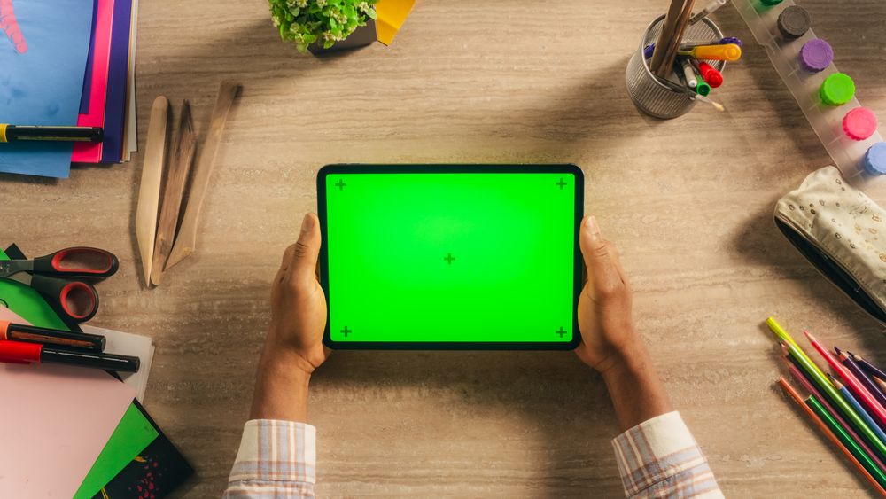Creative Multiethnic Black Artist Holding Tablet with Green Screen Mock Up Display Above a Desk with Art Supplies. Photo Template for Digital Presentation, Design Content Creation and Tutorials