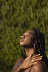 Close-up portrait of a young Black woman resting her hand over her shoulder with her eyes closed