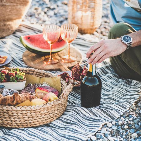 Man with hand on bottle of wine at outdoor picnic, square crop