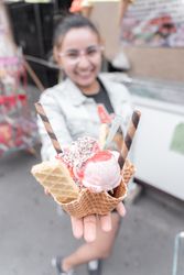 A young Hispanic woman is smiling holding a traditional ice cream in front of a street market stall