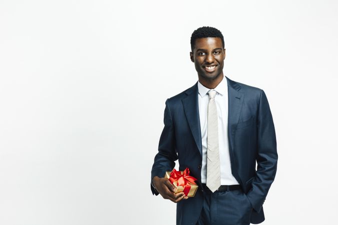 Professionally dressed Black man holding present wrapped in gold paper and red bow