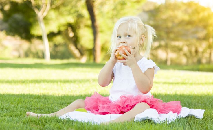 Little Girl In Grass Eating Healthy Apple