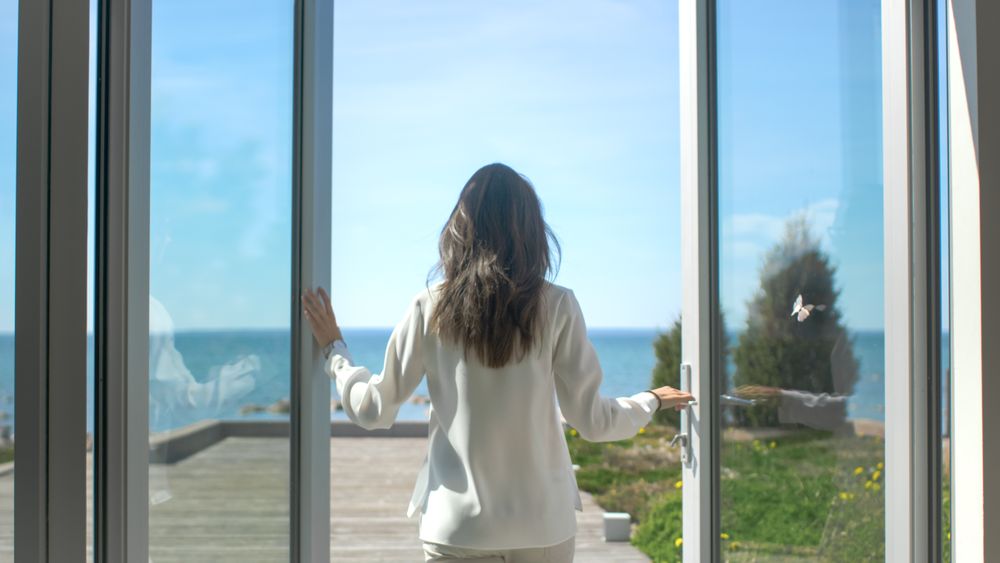 Shot of a Brunette with Loose Hair Opening Doors of the Balcony and Walking onto Sunny Terrace with Seaside View.