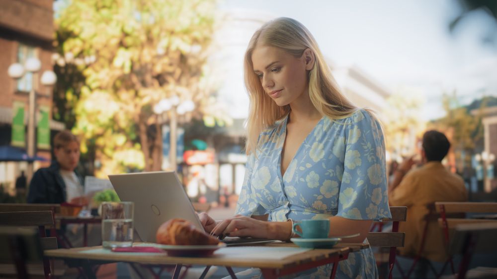 Blond Young Woman in a Blue Dress with Flower Pattern Drinking Espresso While Working Remotely