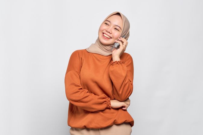 Smiling Muslim woman with smart phone to her ear talking to friend
