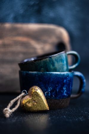 Side view of two blue mugs and golden heart decoration