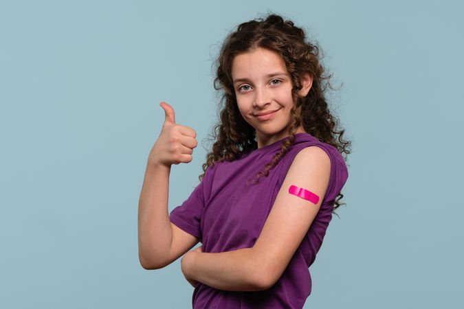 Girl giving thumbs up with bandage on vaccinated arm