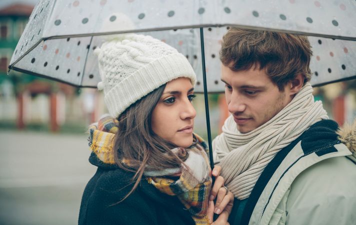 Moody couple facing each other under the umbrella on an autumn rainy day