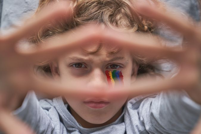 Portrait of boy with rainbow drawing under eye frowning brows