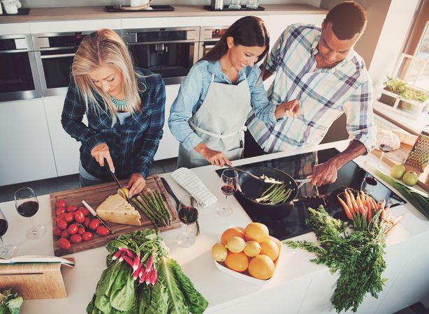 Group of friends cooking vegetables together in the kitchen