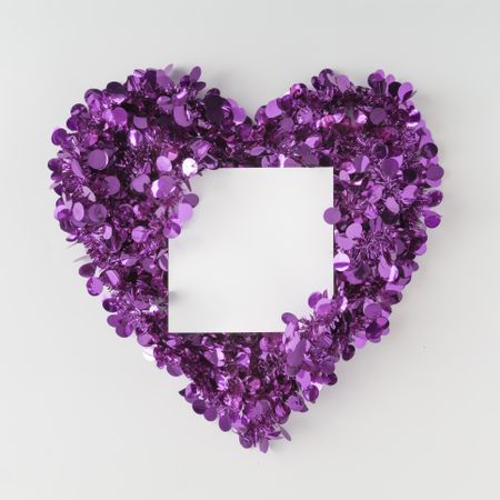 Purple confetti shaped in heart around paper card